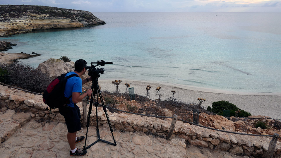 Peter Turek looks through the lens of a camera at a beach in Lampedusa and the blue Mediterranean
