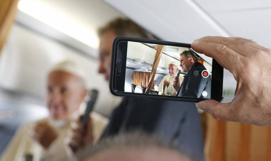 Pope Francis is pictured on a cell phone video with Vatican spokesman, Greg Burke, as he greets journalists aboard his flight from Rome to Vilnius, Lithuania, Sept. 22. (CNS photo/Paul Haring)