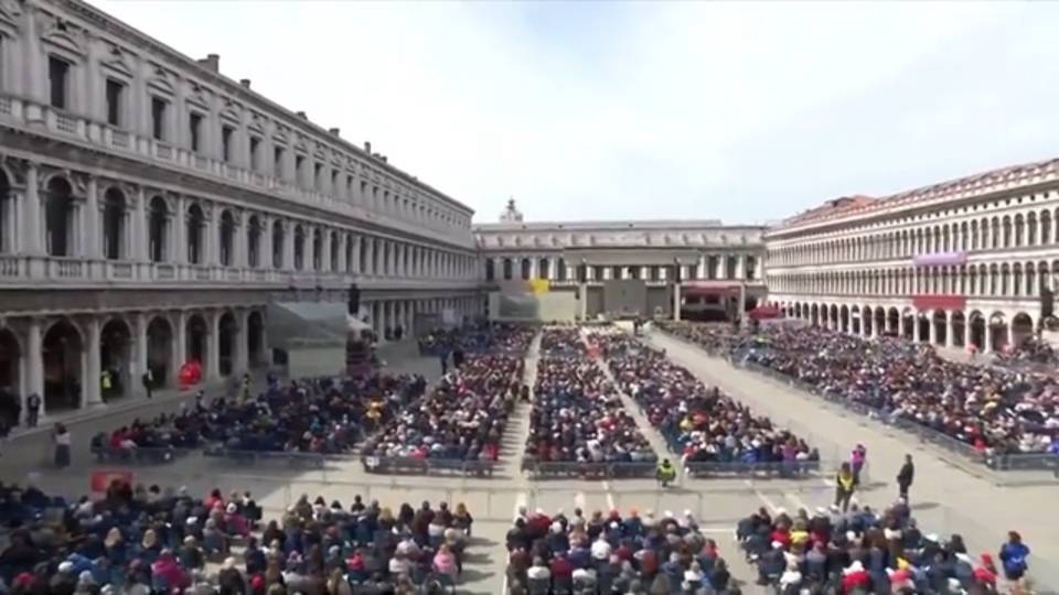 Large crowd in historic square sits in columns listening to Pope Francis' homily.