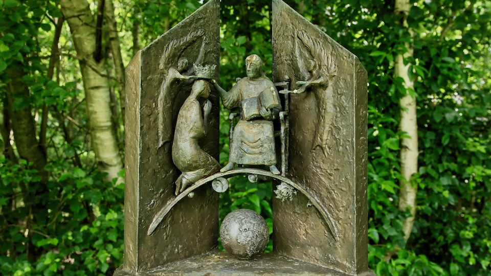 small sculpture of God crowning Mary in front of trees and a globe beneath them.