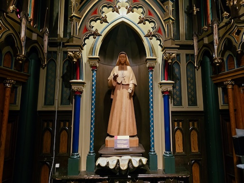 Brown wooden statue of Mother Marie-Rose in a pointed arch niche